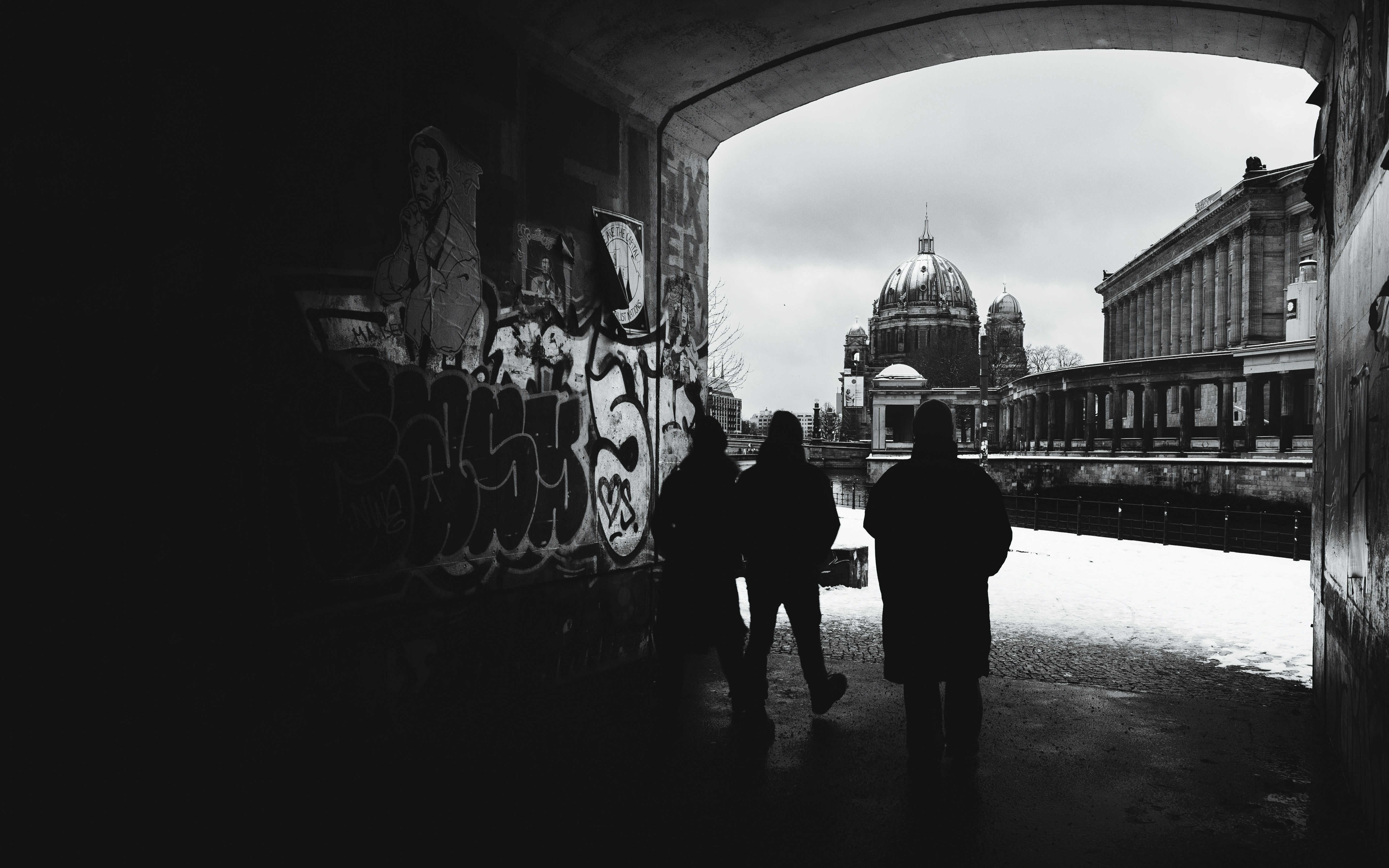 Silhouetted figures in a graffitied tunnel with a cathedral beyond